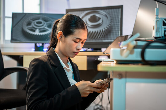 A focused young woman using a smart phone in a modern office with computer screens and office equipment.