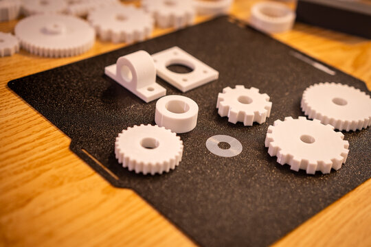 White 3d printed gears and plastic parts arranged on a black mat on a wooden table, showing a prototype and mechanical design concept