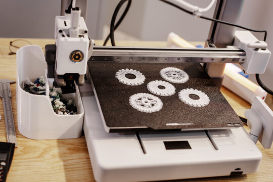 Desktop 3d printer printing white gear parts on the build plate in a workshop