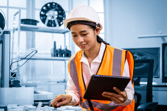 Female engineer in hard hat and safety vest using a tablet in a modern industrial lab or workshop.