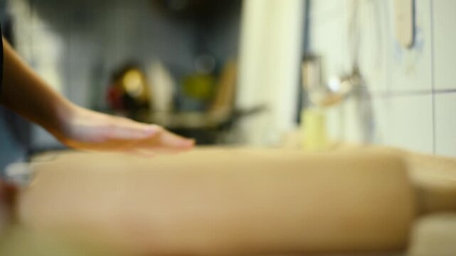 Close up of flattening raw dough sheet with a wooden rolling pin