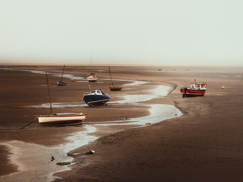 Small fishing boats and sailboats rest aground on the expansive tidal