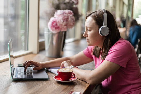 Woman wearing headphones working on laptop in cafe