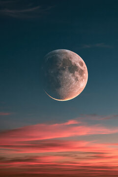 Moon appears in the evening sky with clouds and colors of sunset