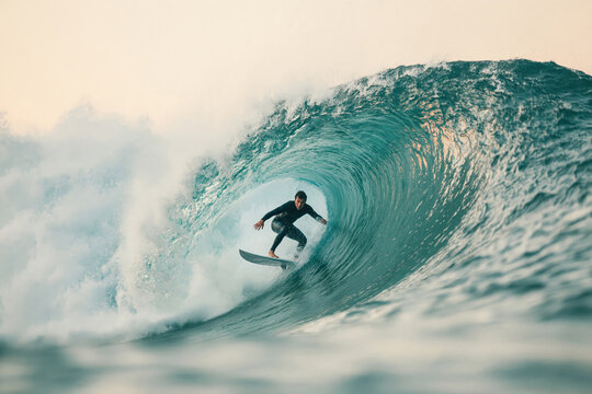 Surfer rides a large wave at sunset in a coastal area with crashing water and bright sky