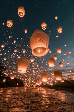 Lanterns floating in the sky during a night festival near a river with a dark blue sky and visible stars