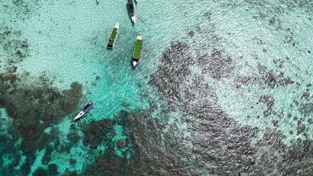 Aerial drone view of tourist boat moored at Kecil Cemara Island in Karimunjawa, Indonesia, featuring turquoise water, white sandy beach and tropical marine landscape.