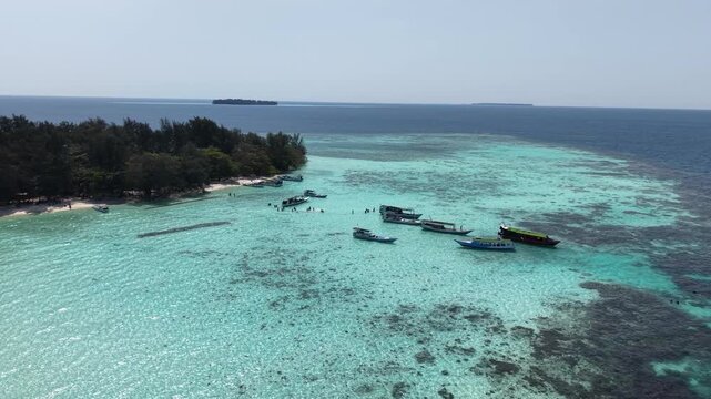 Aerial drone view of tourist boat moored at Kecil Cemara Island in Karimunjawa, Indonesia, featuring turquoise water, white sandy beach and tropical marine landscape.