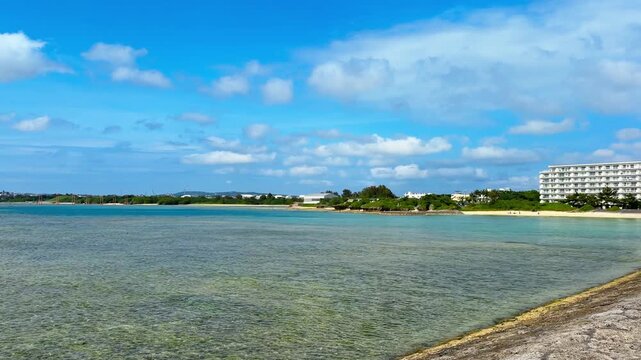 Coastal Buildings Line The Shoreline Beside A Shallow, Serene Sea Along Sunabe Seawall In Okinawa, Japan. Panning Left Shot