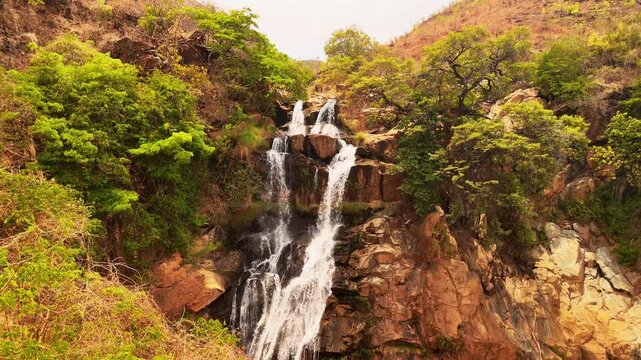 Slow motion drone view pulling back from a beautiful waterfall cascading over reddish rocks amid lush greenery near Usisya, Malawi.