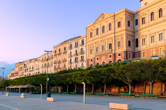 A beautiful clean street post colonial architecture epoch buildings bathed in warm sunlight lined with mature trees and public seating