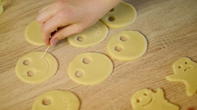 Drawing a smiling mouth on a raw cookie dough cutout with toothpick