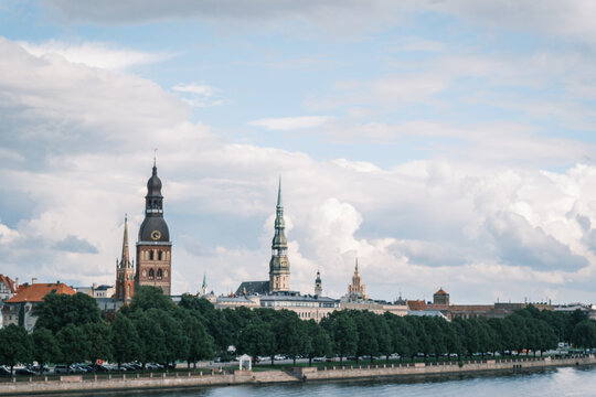 Panoramic view of Riga Old Town church spires and Riga Cathedral skyline rising above trees under dramatic clouds along Daugava River, Latvia