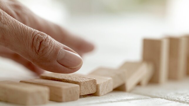 Hand stopping falling dominoes in a line, symbolizing risk management and stopping negative consequences