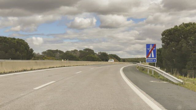 Highway curve through green countryside with a motorway sign marking the end of motorway section ahead.