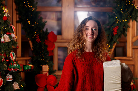 Smiling woman in red sweater holding gift box in festive Christmas room