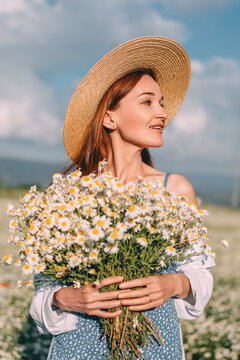Springtime joy captured as young woman wears straw hat while holding Matricaria chamomilla flowers in sunny meadow