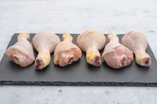 Raw chicken drumsticks arranged on slate serving board
