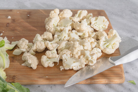 Chopped cauliflower florets on wooden board with knife