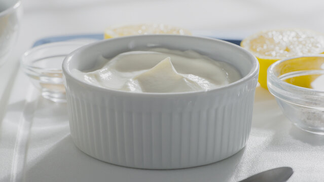 Bowl of thick creamy yogurt is placed on a white surface with lemon