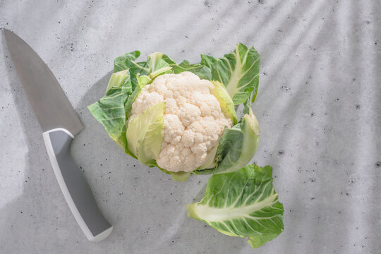 Whole cauliflower with knife on light kitchen surface