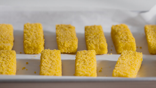 Golden breaded fish sticks are lined up in even rows on parchment paper