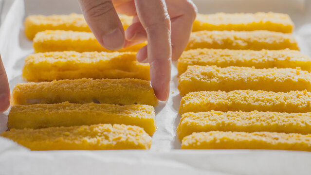Fingers carefully place breaded fish sticks in neat rows on a tray.