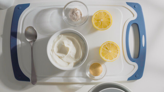 A cutting board displays yogurt, lemon, salt, and seasoning for making sauce.