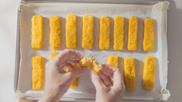 A person breaks a breaded fish stick in half to reveal the white filling inside.