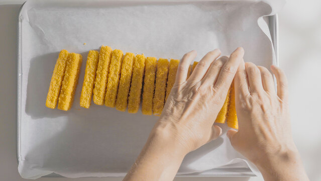 Breaded fish sticks are arranged in neat rows on parchment paper ready for the oven.
