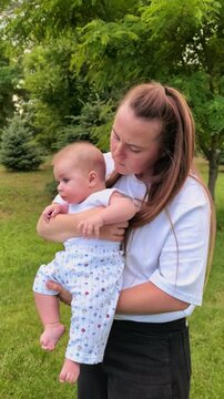 Caring mother holds her infant in her arms outdoors in a green park, maternal love, family bonding and peaceful summer lifestyle.