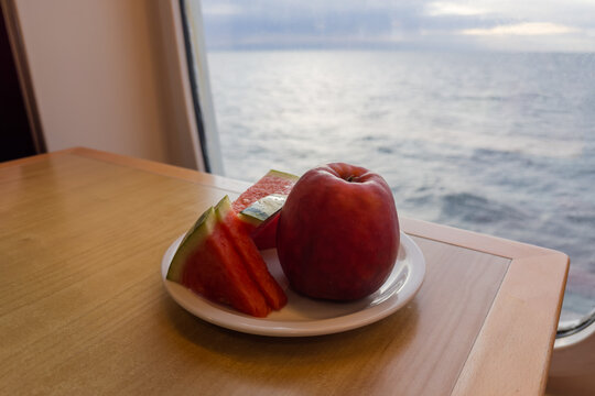 Watermelon slices and red apple on plate against sea view