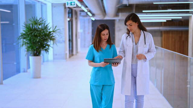 Medical professionals collaborating on digital tablet in hospital corridor