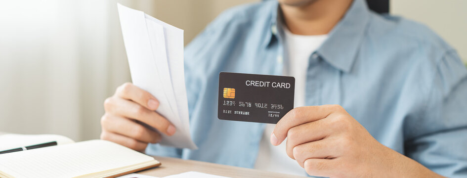Asian young man holding credit card and bills while using a calculator to calculate monthly expenses, financial planning, debt management and personal budget concept.