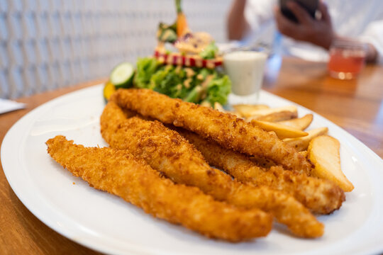 Plate of crispy fish fingers with potato wedges and a fresh salad served on a wooden table.