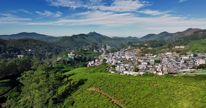 Aerial view of the lush green tea plantations of Munnar, Kerala, covering rolling hills under a bright blue sky with scattered clouds, the scenic beauty of this popular hill station in South India.