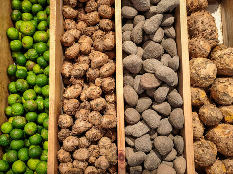Fresh Traditional Spices and Roots Market Display. Vibrant wooden trays featuring fresh kaffir limes, ginger roots, kluwek nuts, and aromatic tubers at a local spice bazaar.