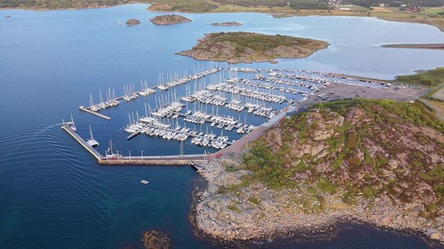 Aerial view of Sando marina filled with numerous sailboats docked in calm blue water surrounded by rocky coastline and green landscape in Vallda, Hallands lan, Sweden.