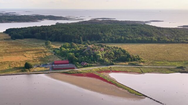 Aerial view of Sando with red farm buildings, green fields, and coastal waters in Vallda, Hallands lan, Sweden.
