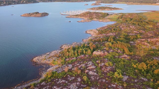 Aerial view of the rocky coastline and marina at Vallda Sando Naturreservat with lush greenery and calm blue waters in Vallda, Hallands lan, Sweden.
