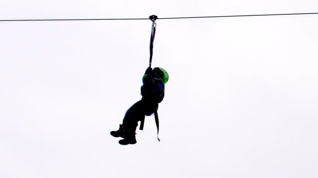 Brave boy likes riding on zip-line at adventure park. Child enjoys riding on high zip-line at adventure park against grey winter sky