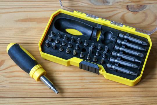 Open screwdriver set with interchangeable bits and handle in yellow case on wooden table for home repair and DIY work.