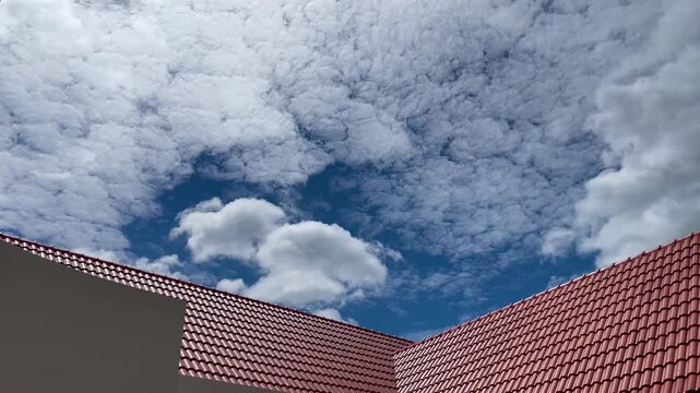 Blue sky with fluffy clouds above red tiled house roof
