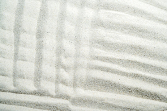 Minimalist white sand texture featuring raked Zen garden patterns with clean lines. Summer, natural or texture background