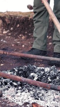 Person working with a shovel outdoors near hot coals and ash outdoors close-up shot of a using a metal to manage and wood on the ground fire outdoor ground tool dirt