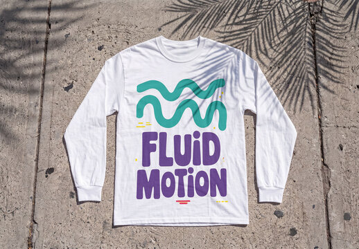 Mockup of A white long sleeve t-shirt is laid flat on a concrete surface. Shadows from palm leaves are cast on the shirt.