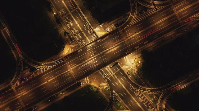 Aerial top down view of a city highway interchange at night with moving cars and bright lights
