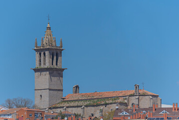 Obraz premium Historic Spanish stone church with Gothic bell tower and moss-covered tiled roof overlooking town rooftops.