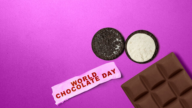 High-angle shot of a chocolate bar, sandwich cookies, and a 'World Chocolate Day' paper sign on a glittery purple background. World Chocolate Day celebration