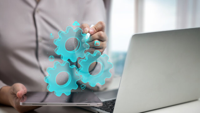 Professional woman using a digital tablet and laptop with virtual glowing gears, representing business automation, system integration, and workflow optimization. Data and automation concept